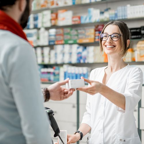 Eine Apothekerin überreicht einem Kunden ein Medikament